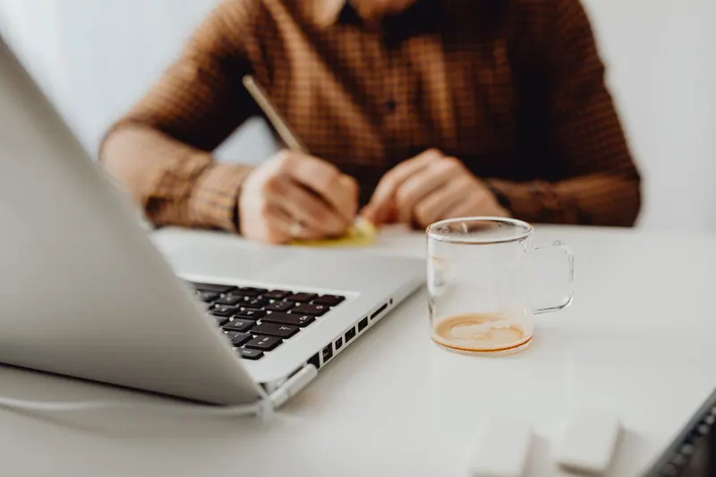Persona escribiendo un correo en un portátil con una taza de café
